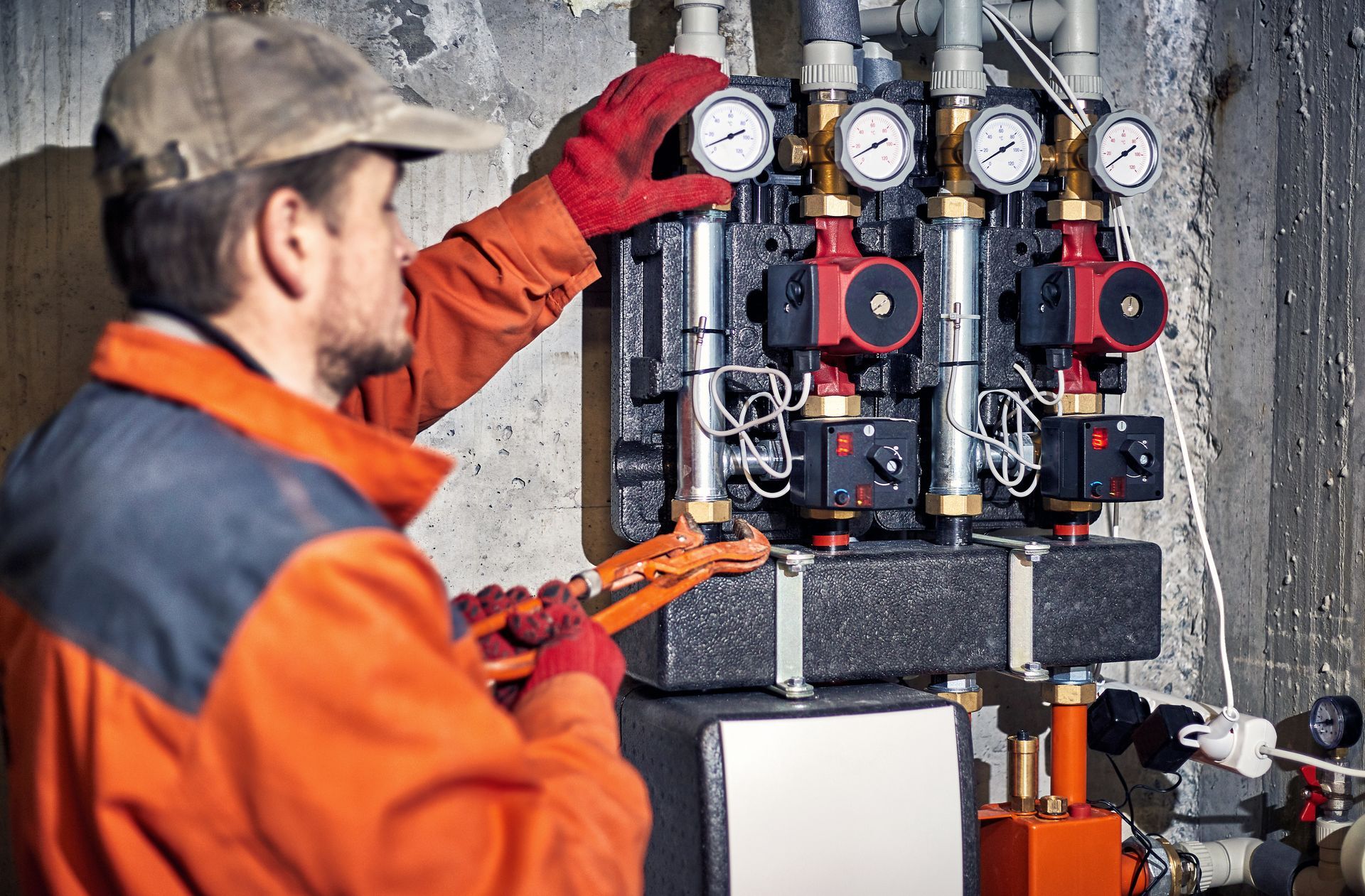 Technicien en veste orange ajustant les manomètres sur des équipements de tuyauterie et de contrôle industriels à l'intérieur d'un bâtiment.