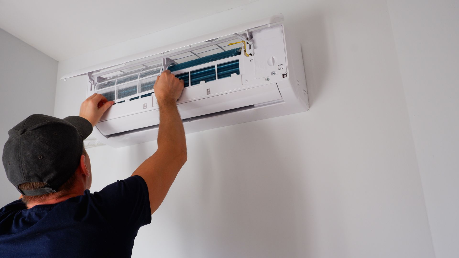 Mains installant une grille d'aération blanche sur un mur carrelé gris.
