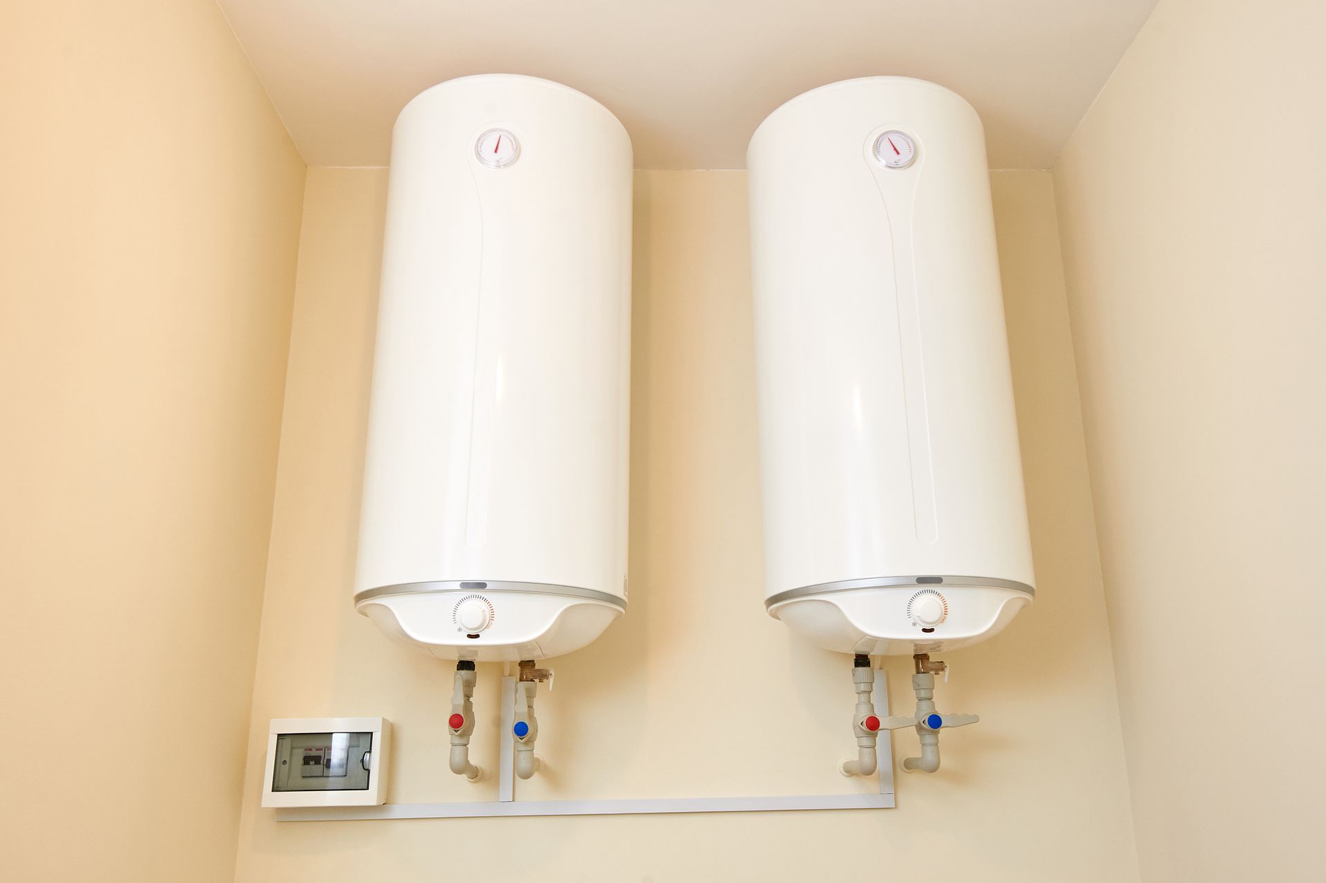 Deux chauffe-eau muraux blancs au-dessus d'un thermostat dans une buanderie beige.