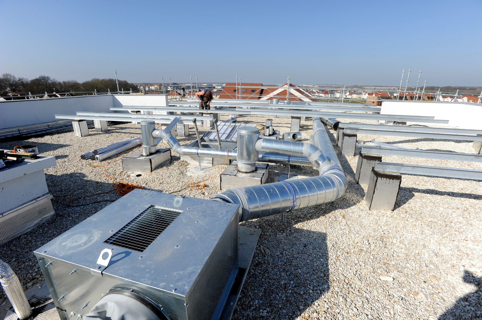 Équipements et conduits de ventilation sur un toit plat recouvert de gravier, sous un ciel bleu dégagé.