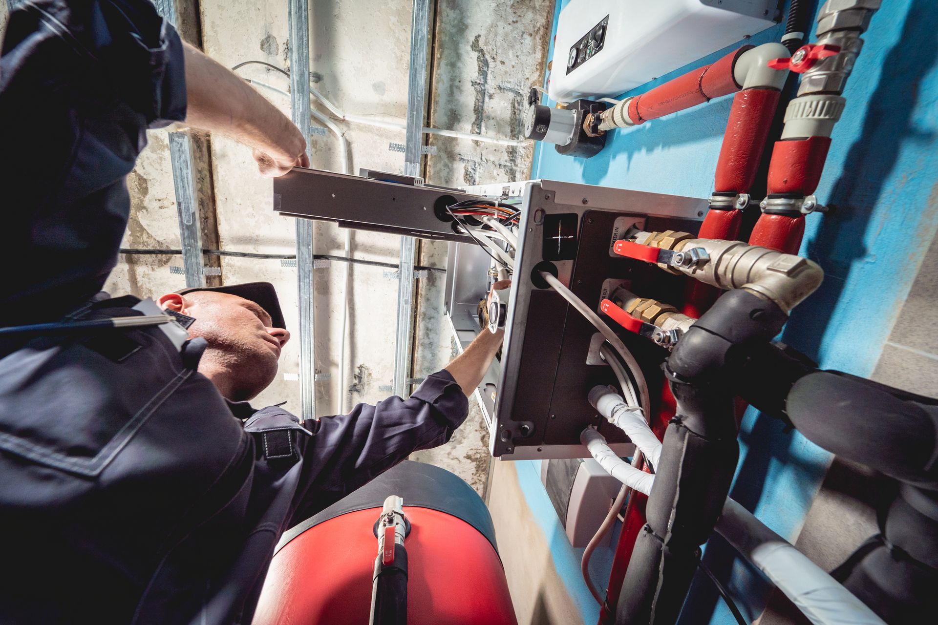 Un technicien inspecte les tuyaux et les vannes dans un local technique aux dalles de sol bleues.