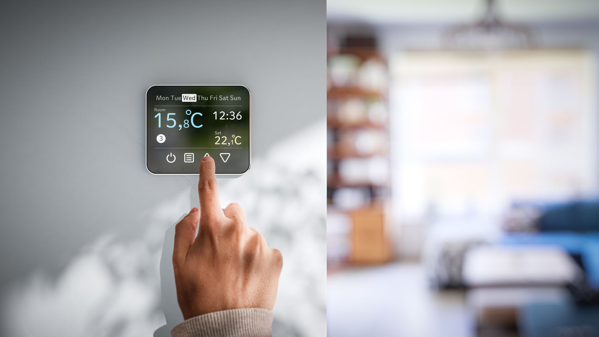 Une main ajuste un thermostat à écran tactile, avec un salon flou en arrière-plan.