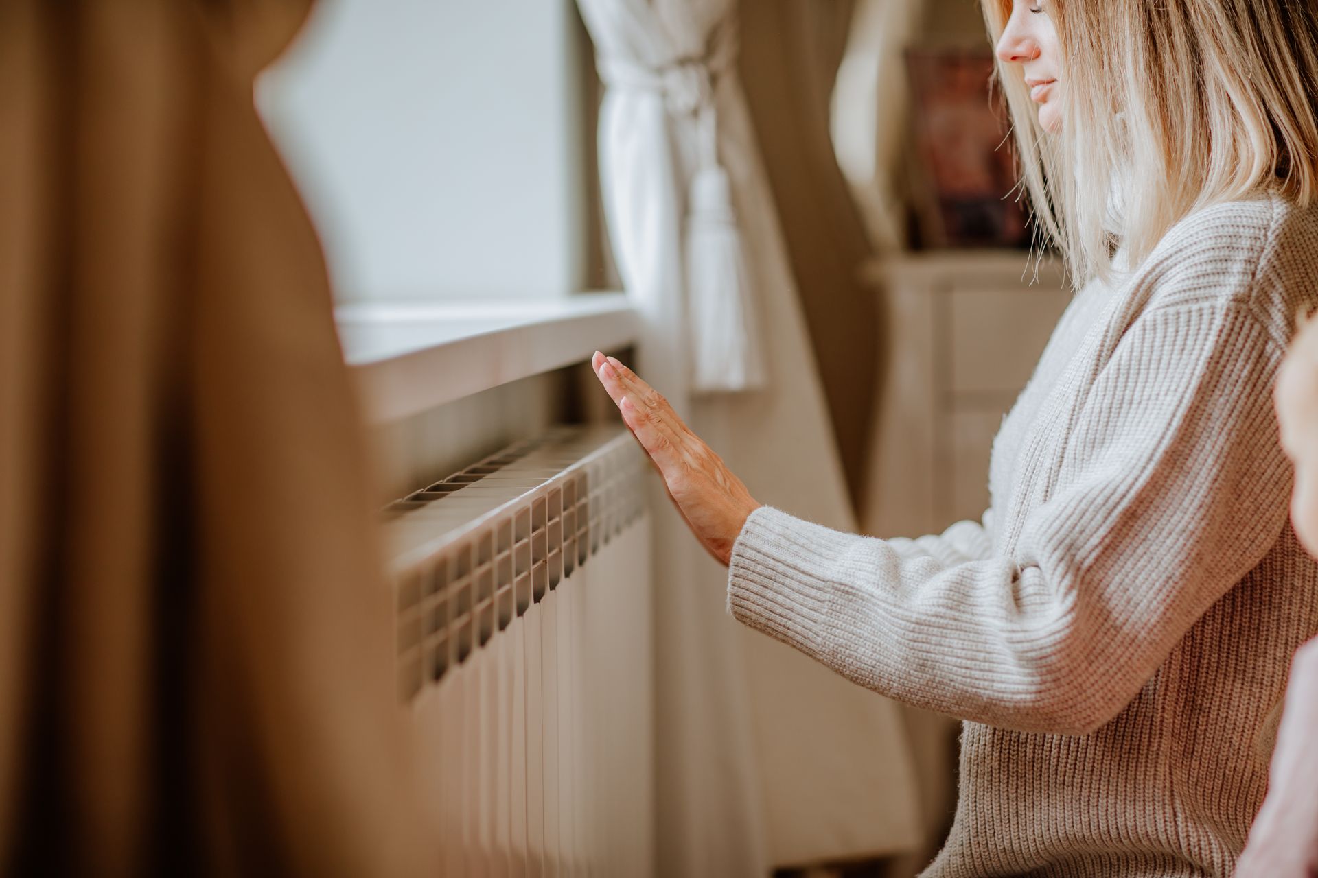 Une personne touche un radiateur près d'une fenêtre dans une pièce faiblement éclairée.