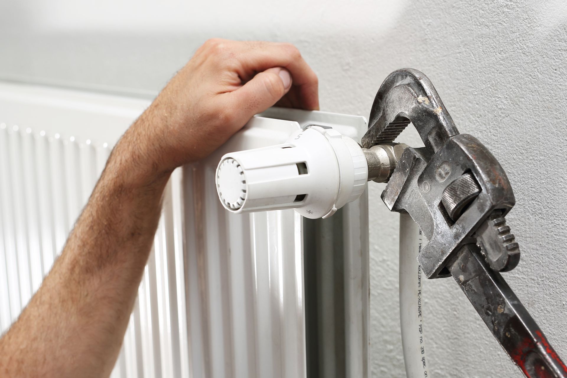 Gros plan d'une main ajustant un robinet de radiateur blanc à l'aide d'une clé.