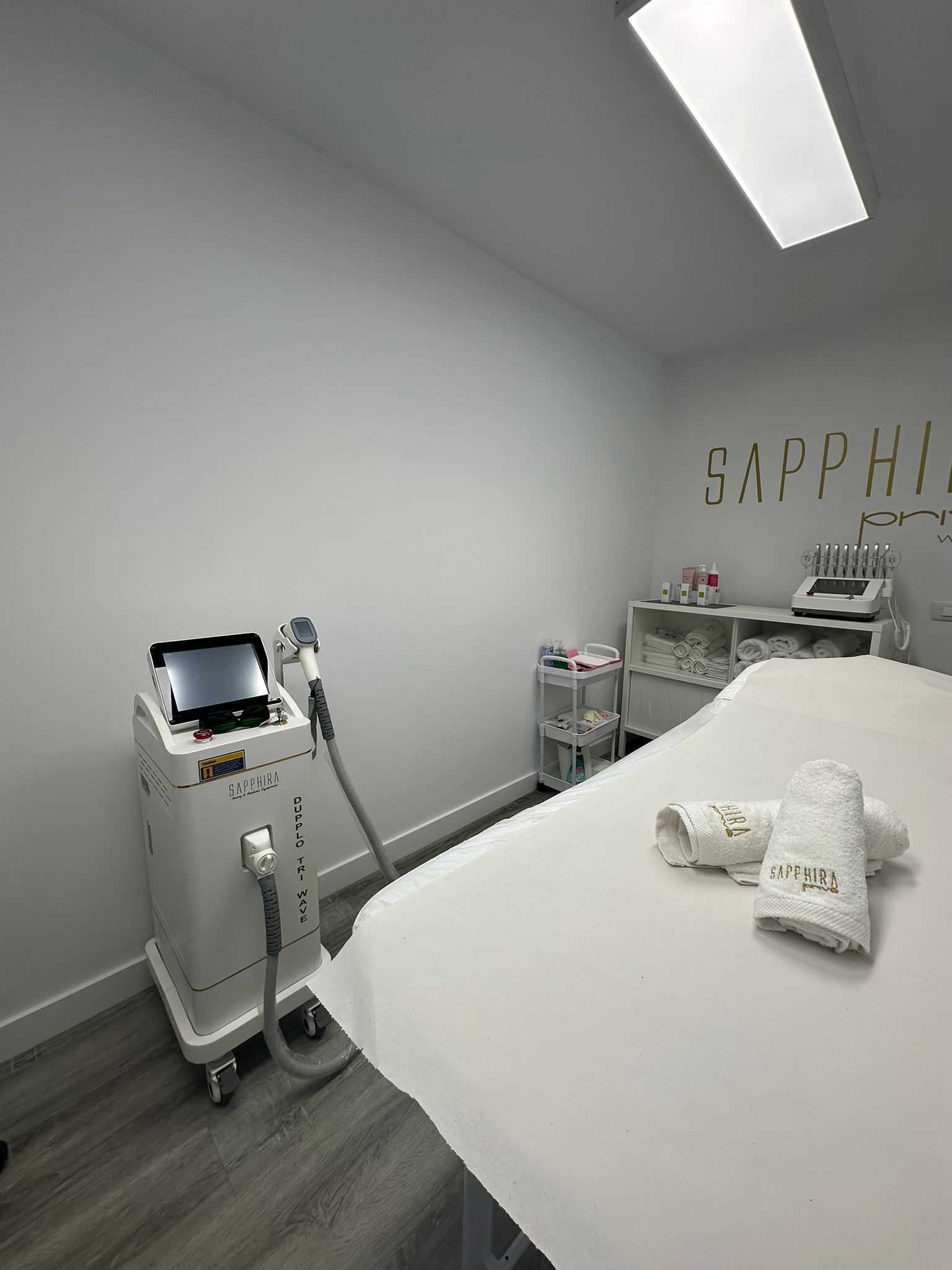 Interior de una sala de spa médico blanca. Cuenta con una camilla de tratamiento, equipo y el logotipo 