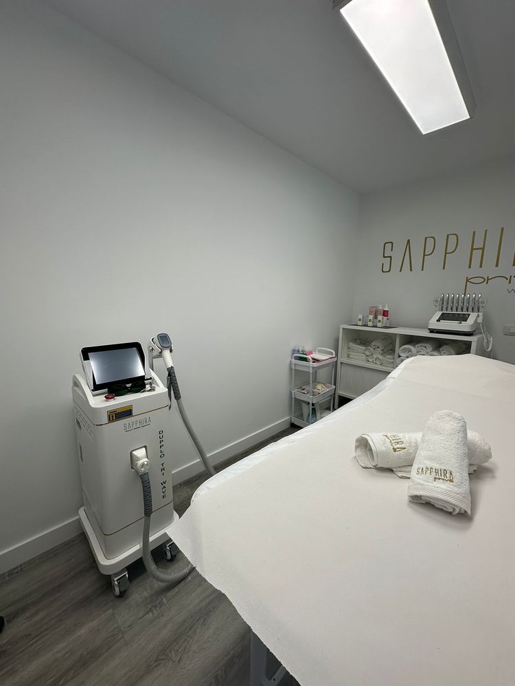Interior de una sala de spa médico blanca. Cuenta con una camilla de tratamiento, equipo y el logotipo