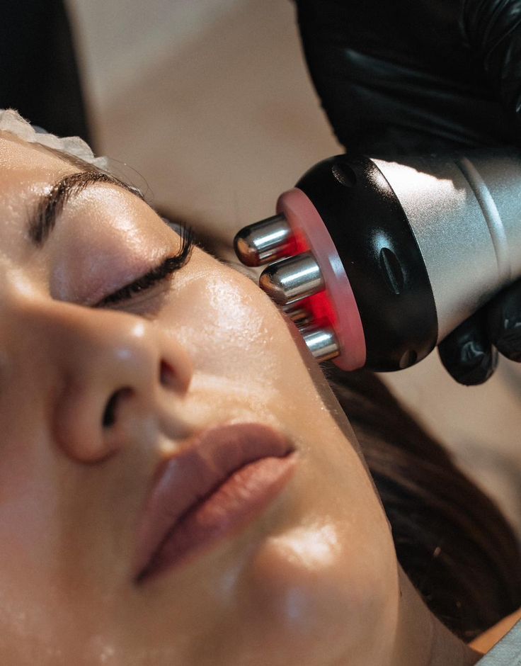Mujer sometiéndose a un tratamiento de cuidado de la piel con un dispositivo portátil que emite luz azul en un spa.