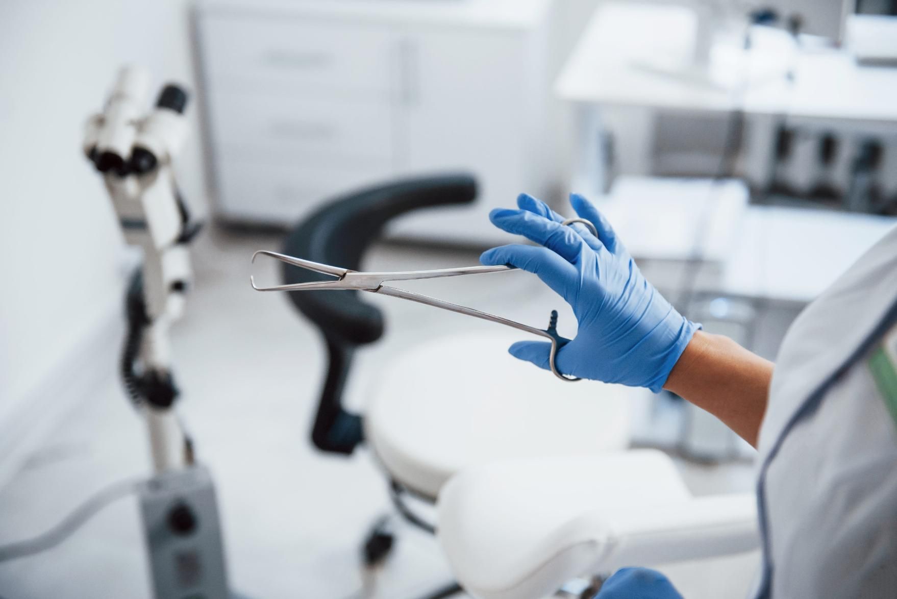Una mano enguantada de azul sostiene un instrumento dental en una luminosa clínica dental