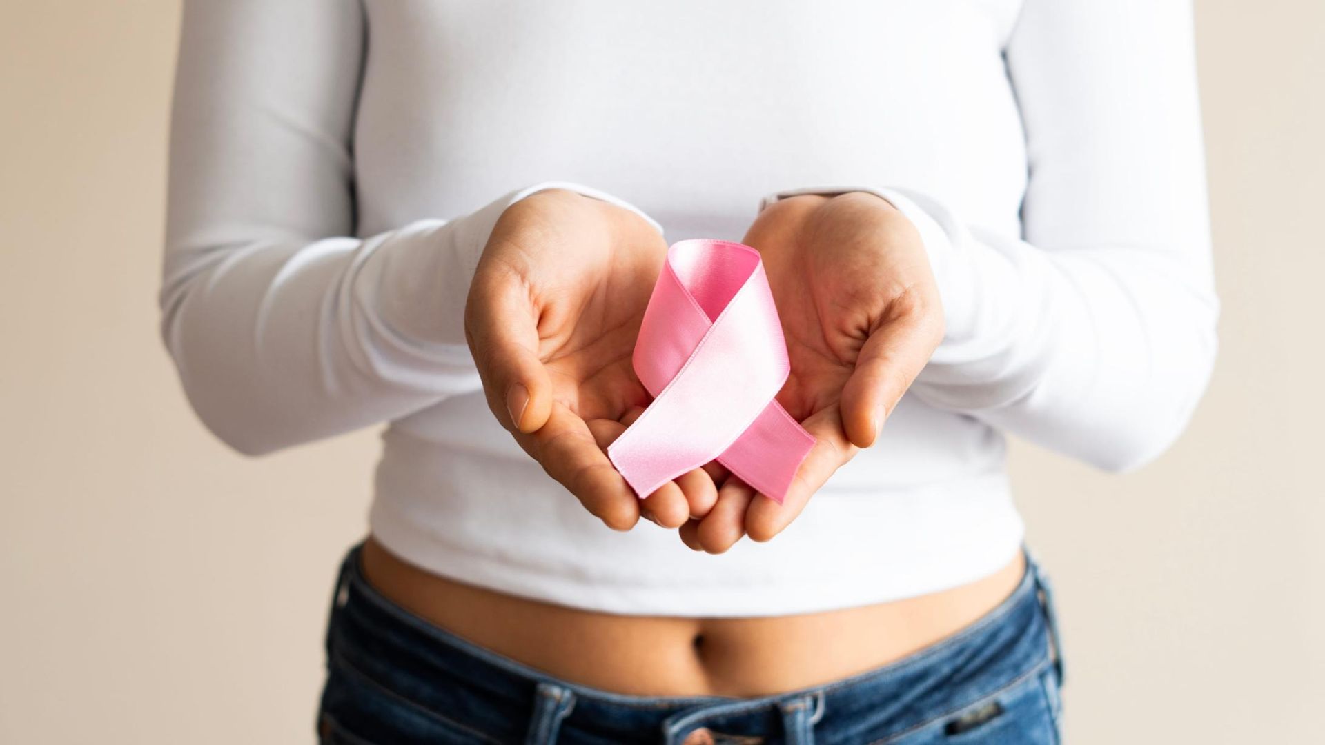 Manos sosteniendo una cinta rosa sobre una camisa blanca y jeans, simbolizando la concienciación sobre el cáncer de mama.
