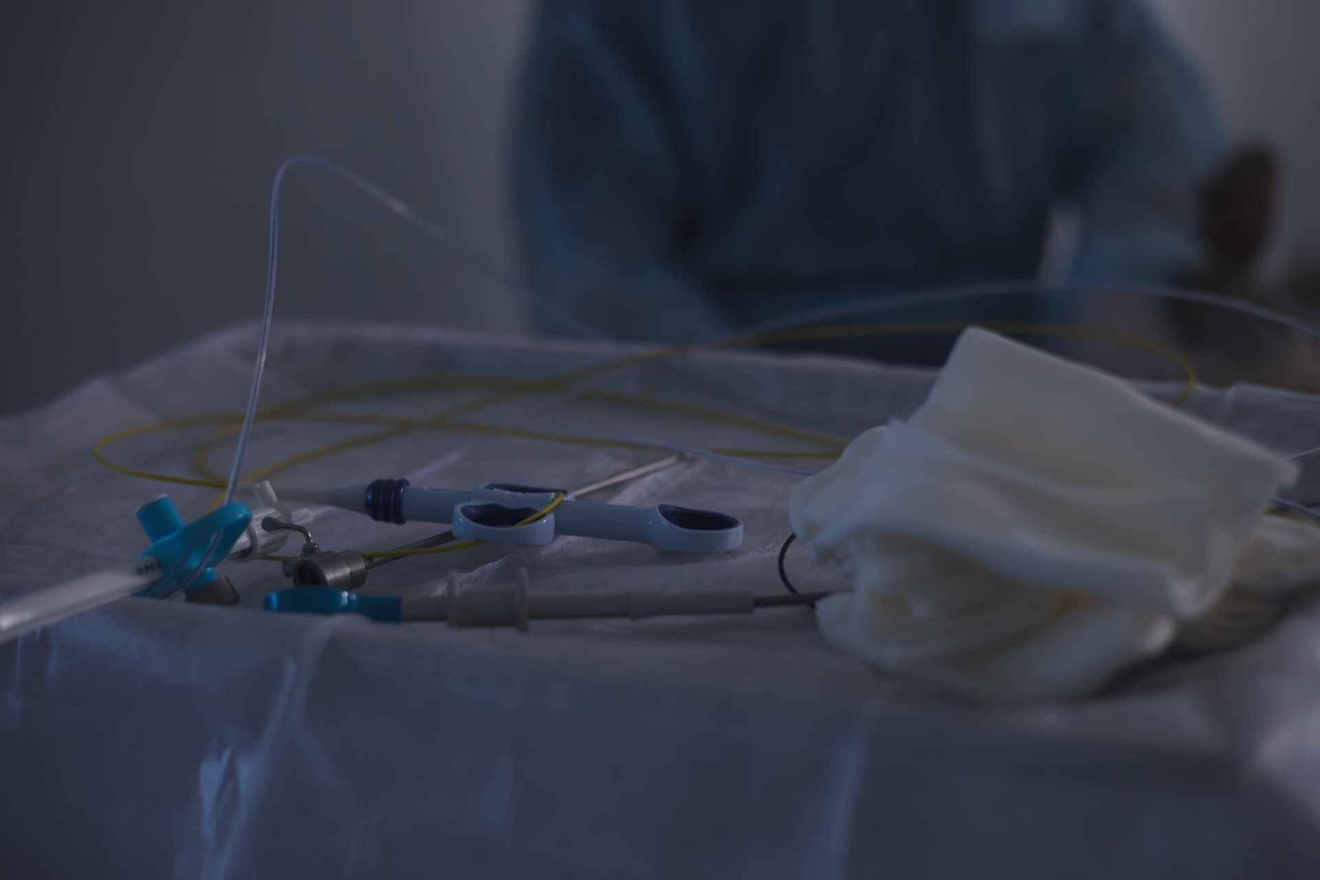 Cama de hospital con tubos médicos y gasas bajo una tenue iluminación azul.