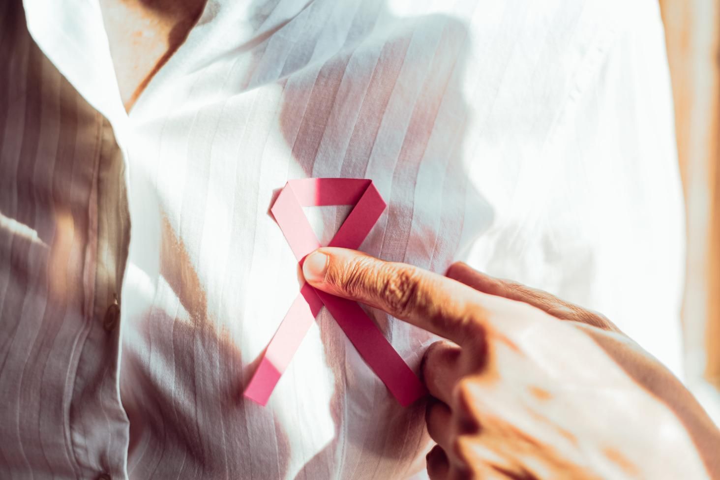 Una mano coloca una cinta rosa de concienciación sobre el cáncer de mama sobre una camisa blanca.
