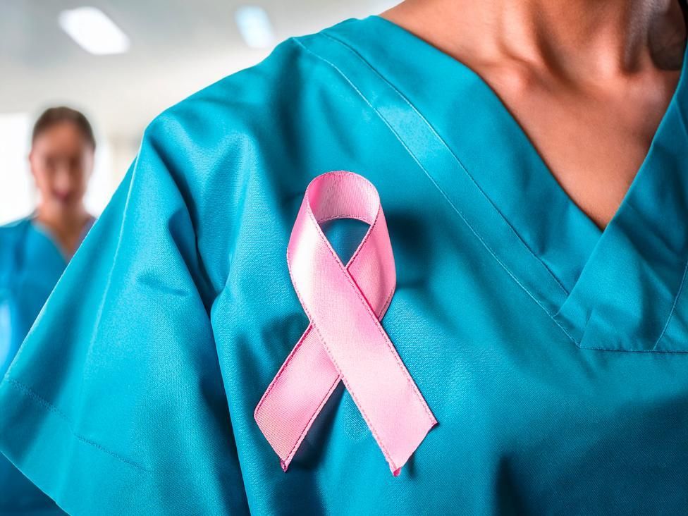 Cinta rosa de concienciación sobre el cáncer de mama prendida a una bata médica turquesa.