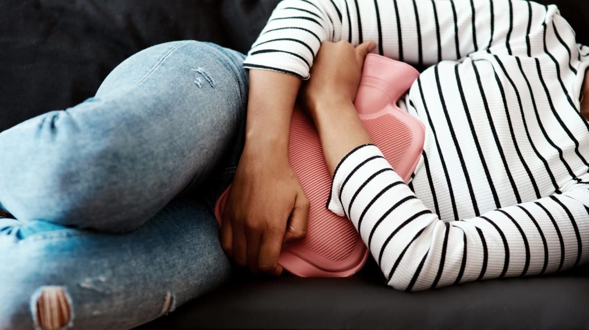 Una persona estaba acurrucada en un sofá, abrazando una almohada rosa, vestida con una camiseta de rayas y vaqueros.