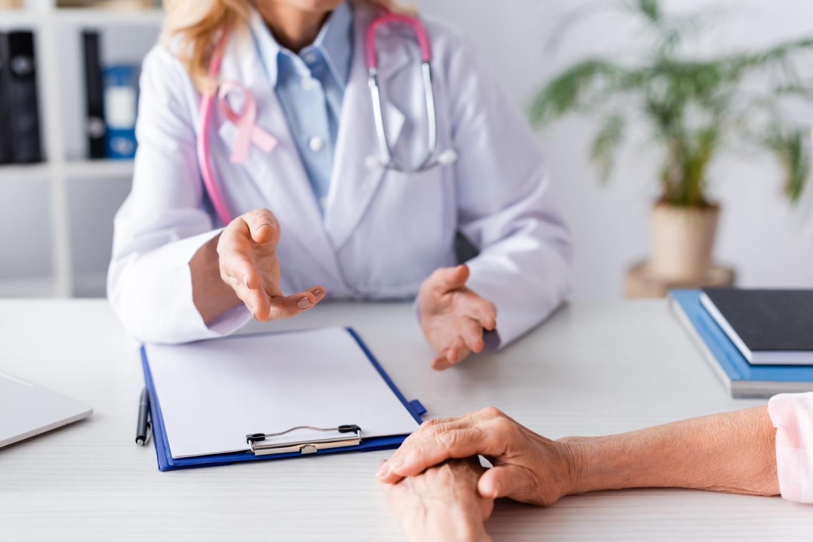 Un médico habla con un paciente sentado en un escritorio, con un portapapeles y un estetoscopio a la vista.
