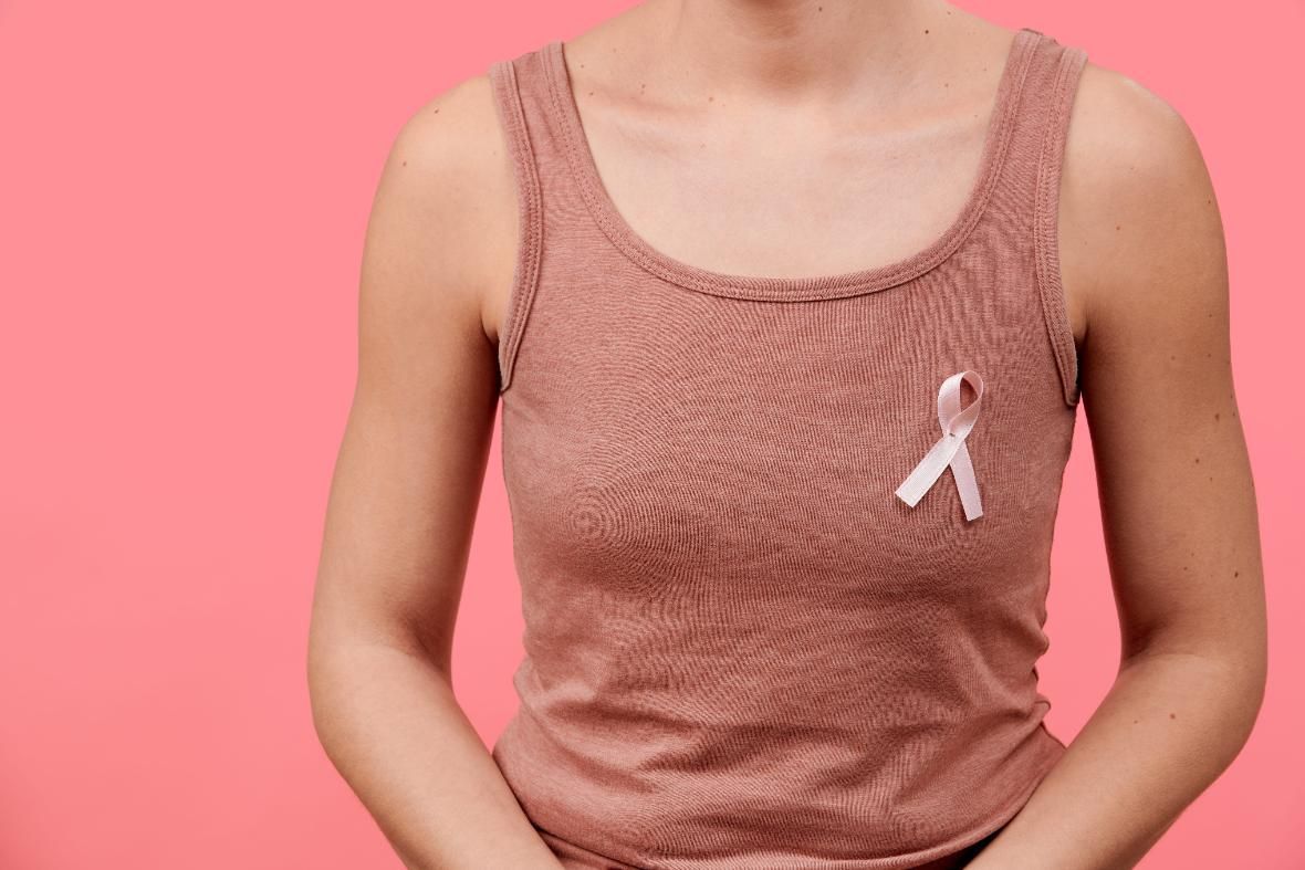 Persona con una camiseta sin mangas rosa con una cinta blanca de concienciación sobre un fondo rosa.