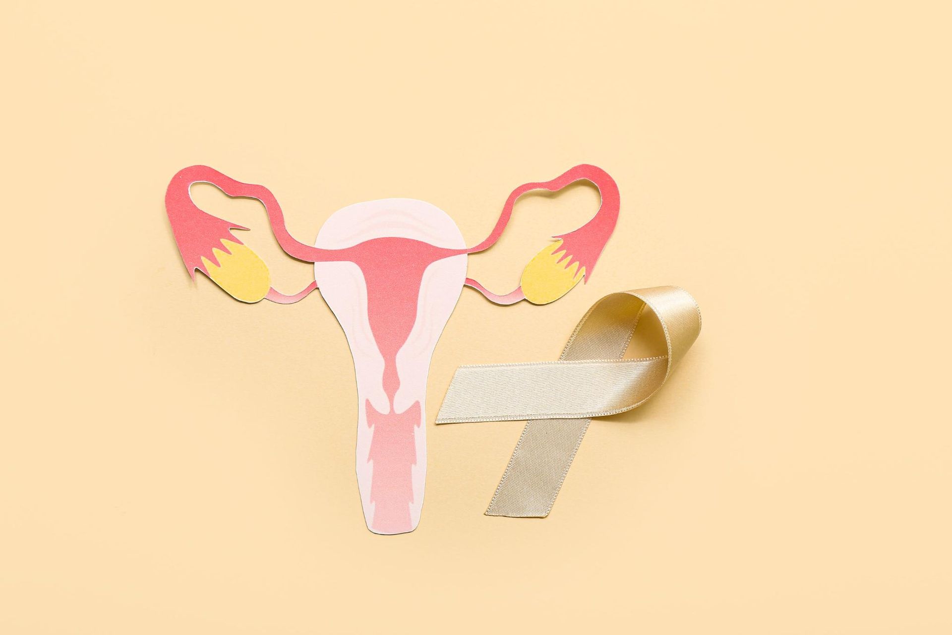 Ilustración de un útero rosa con una cinta dorada de concienciación sobre un fondo beige.