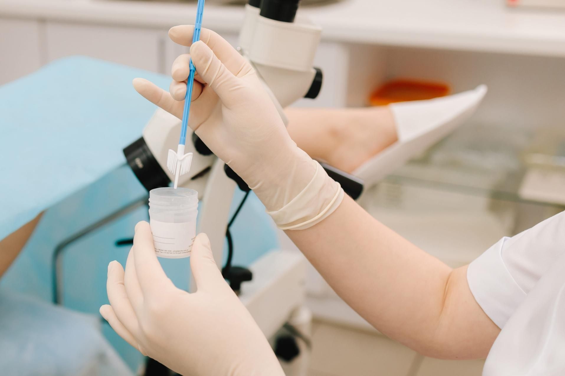 Manos enguantadas pipetean líquido en un pequeño vial en un entorno de laboratorio clínico.
