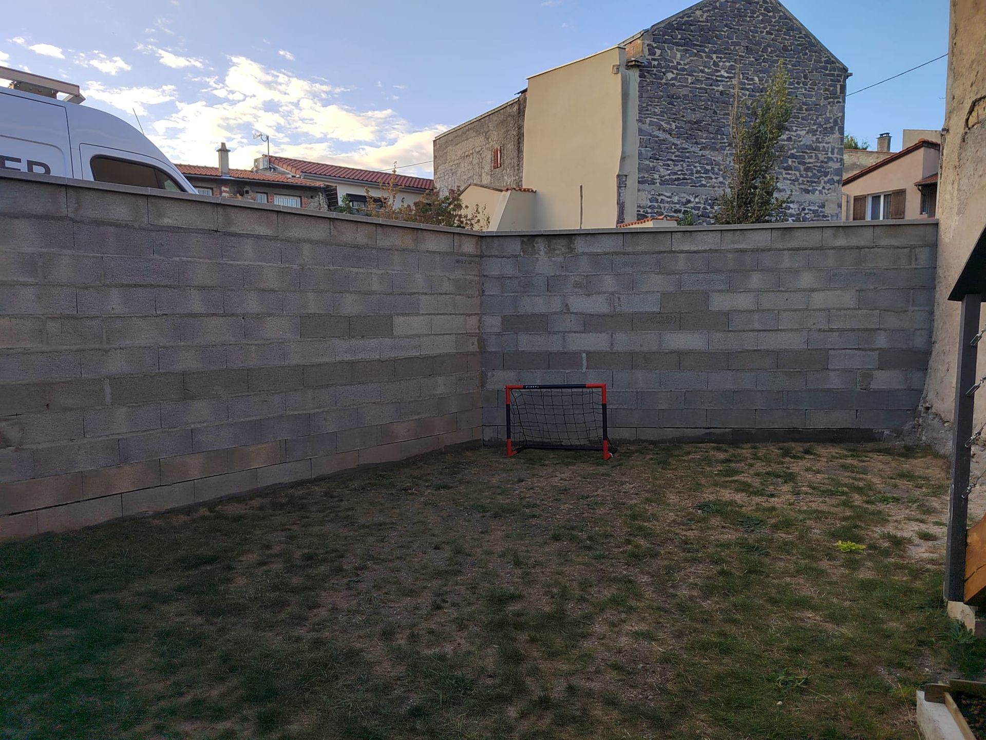 Un petit but de football sur une pelouse entourée de murs en parpaings, avec des bâtiments en arrière-plan.