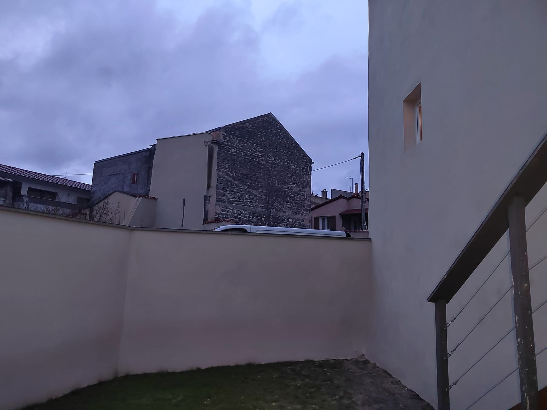 Vue extérieure de bâtiments sous un ciel nuageux. Un mur blanc se trouve au premier plan.