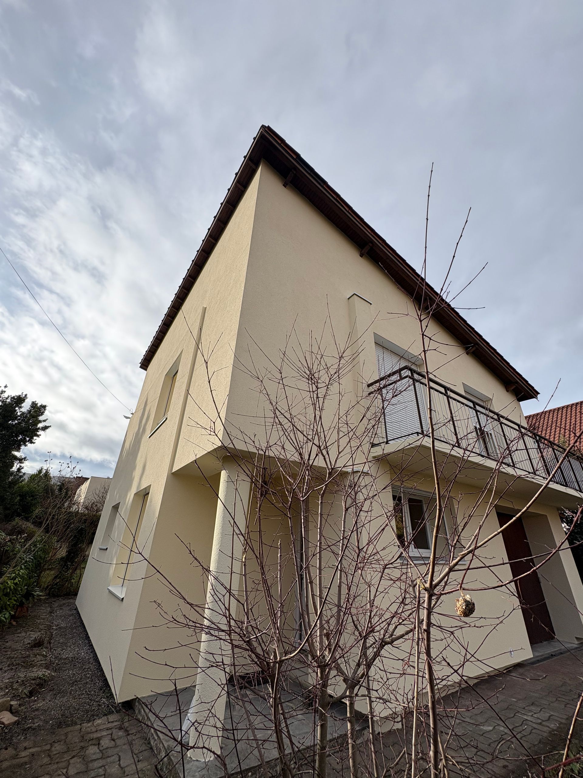 L'extérieur d'un bâtiment avec un mur texturé bleu clair, une gouttière et un toit se détachant sur un ciel nuageux.