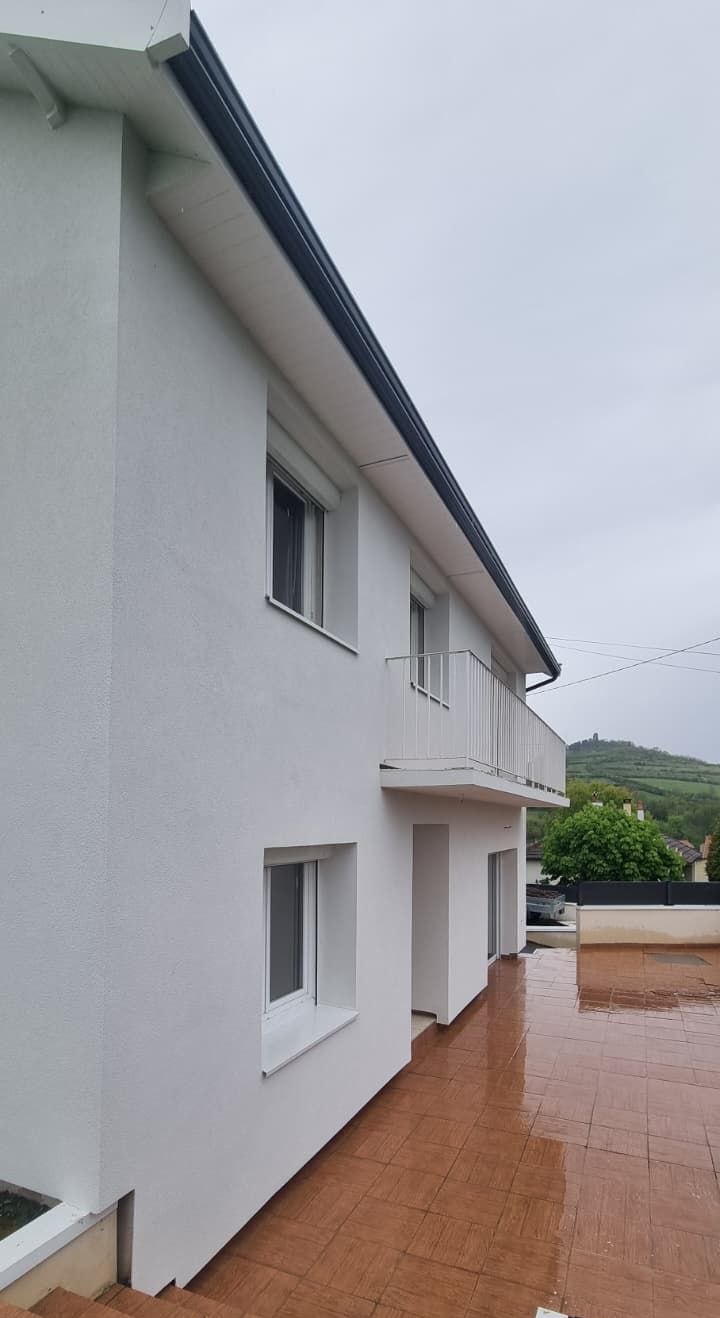 L'extérieur d'un bâtiment avec un mur texturé bleu clair, une gouttière et un toit se détachant sur un ciel nuageux.