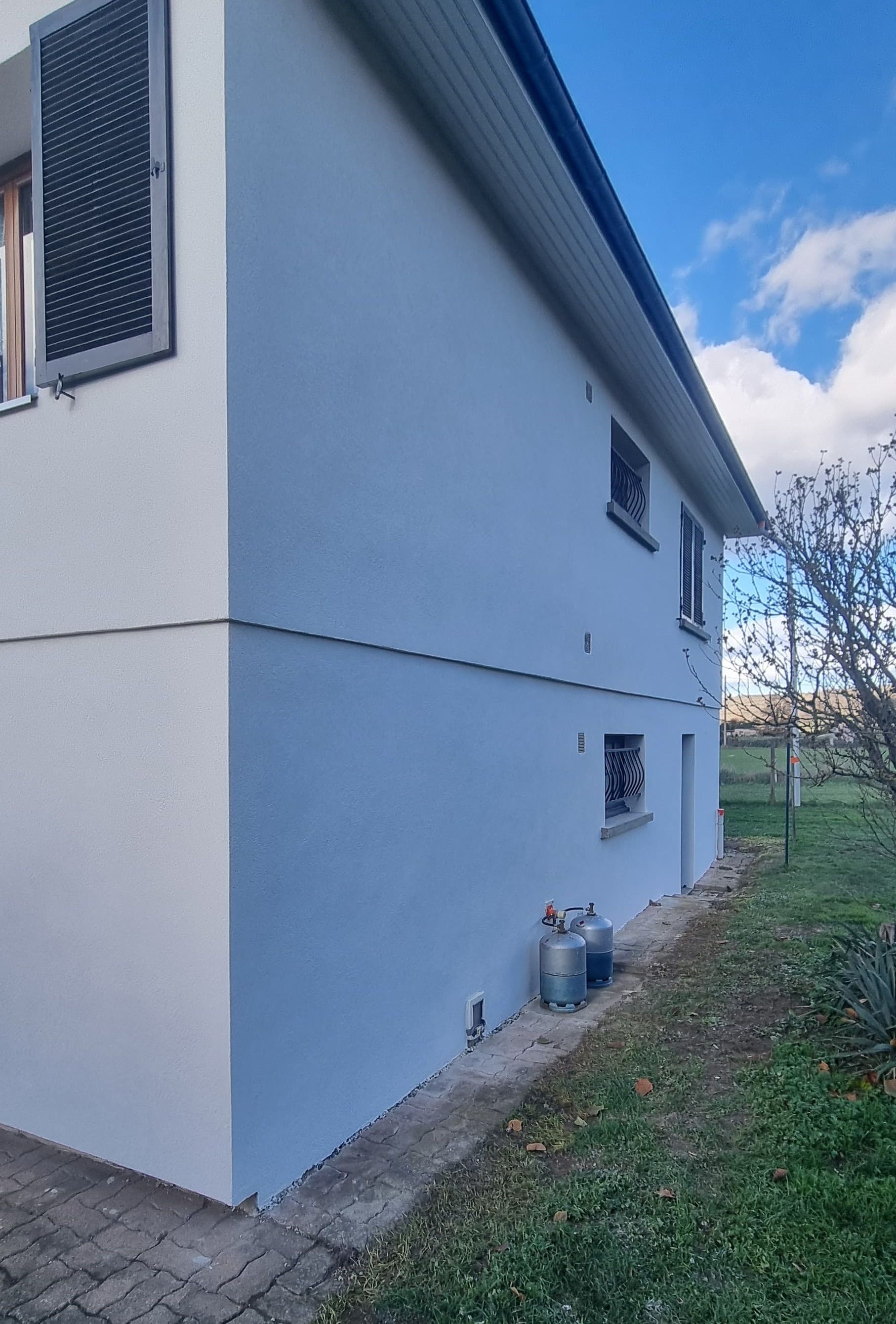 L'extérieur d'un bâtiment avec un mur texturé bleu clair, une gouttière et un toit se détachant sur un ciel nuageux.
