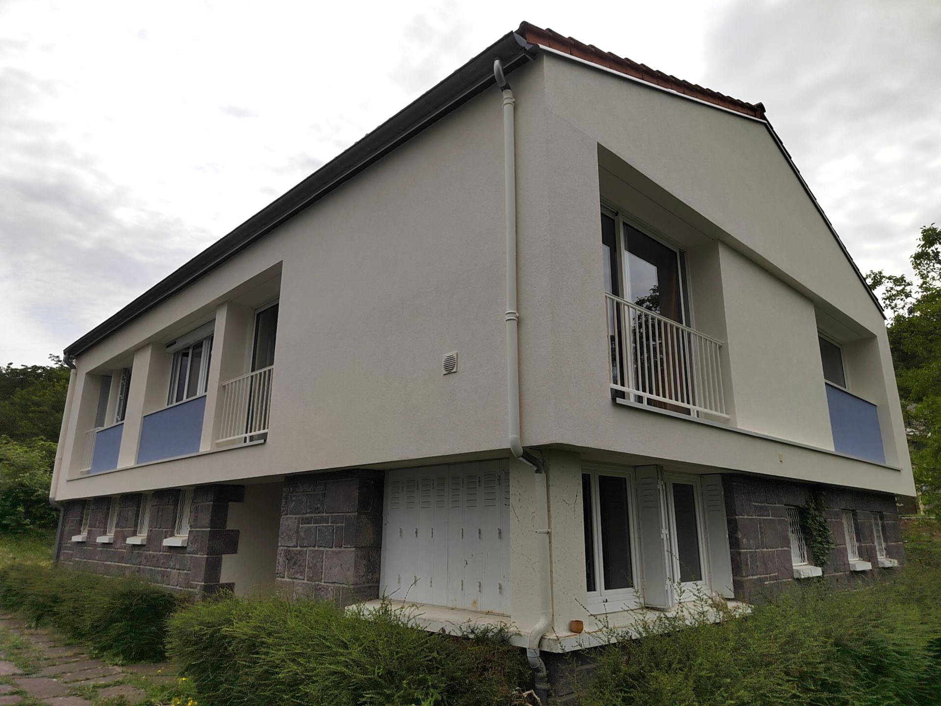 Bâtiment de deux étages avec murs en stuc blanc, soubassement en pierre, petits balcons et fenêtres.