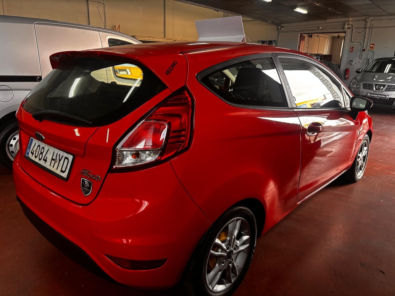 Un Ford Fiesta hatchback rojo estacionado dentro de un garaje, visto desde un ángulo de tres cuartos trasero.