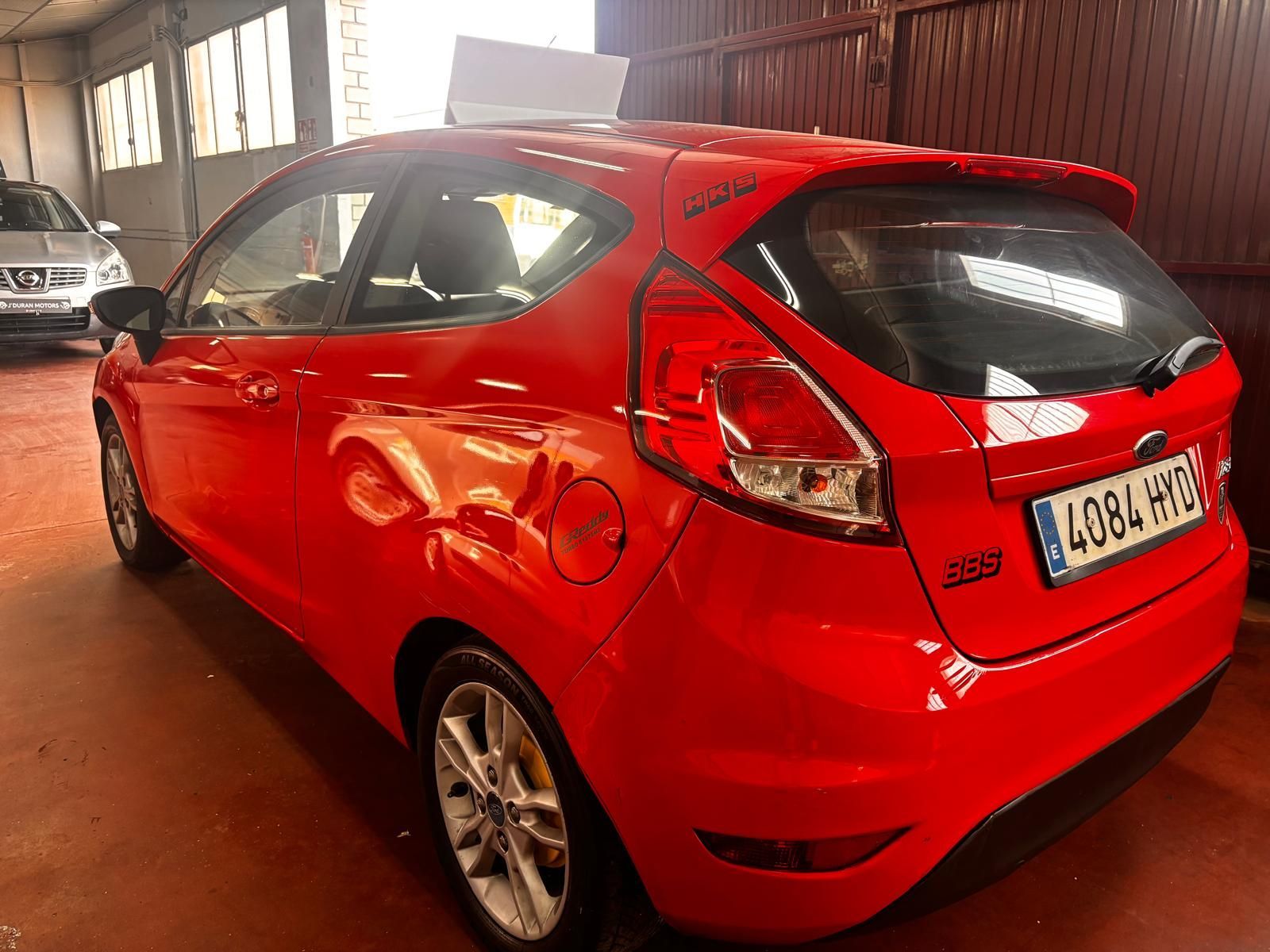 Un Ford Fiesta hatchback rojo de tres puertas estacionado dentro de un garaje con piso de concreto.