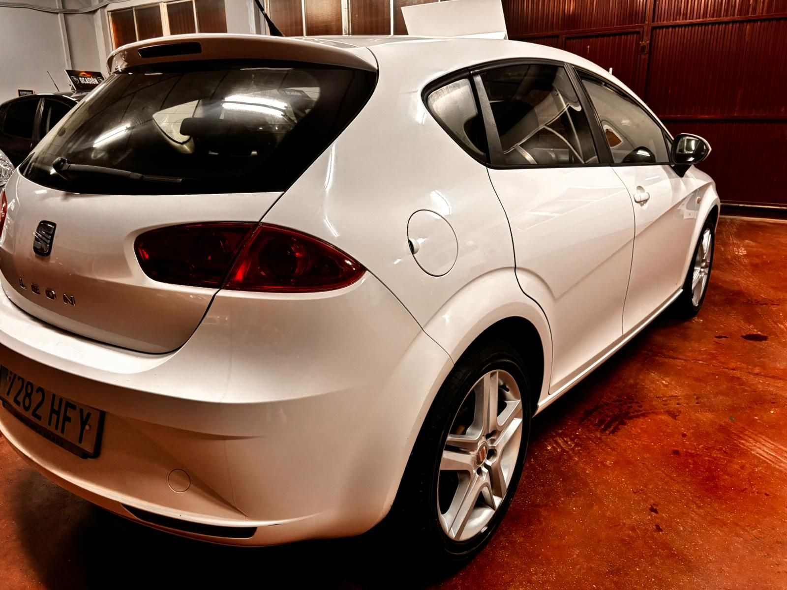 Un SEAT hatchback blanco estacionado dentro de un garaje con suelo de hormigón.