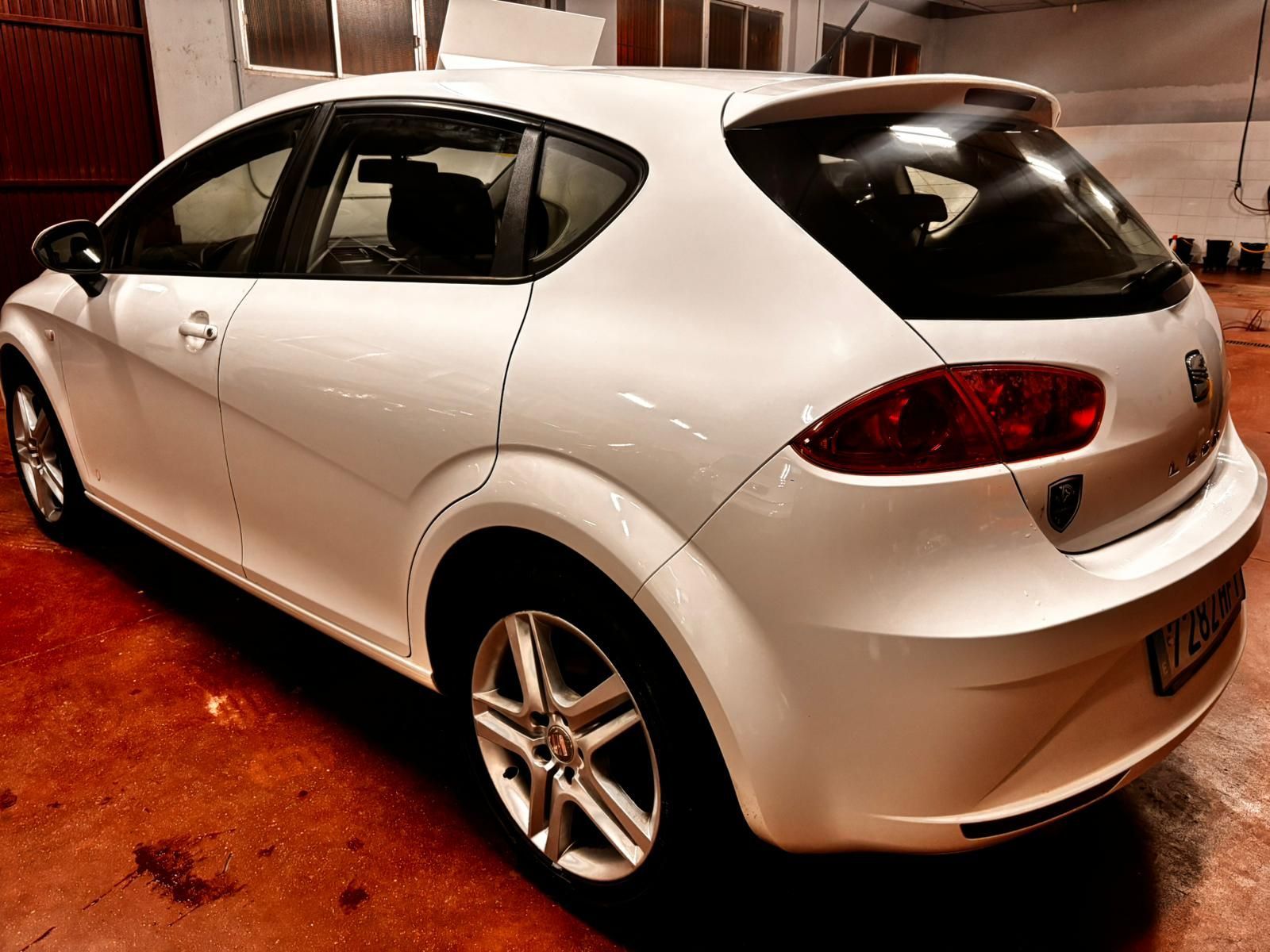 Un SEAT León hatchback blanco estacionado en un garaje con poca luz y suelo de color marrón rojizo.