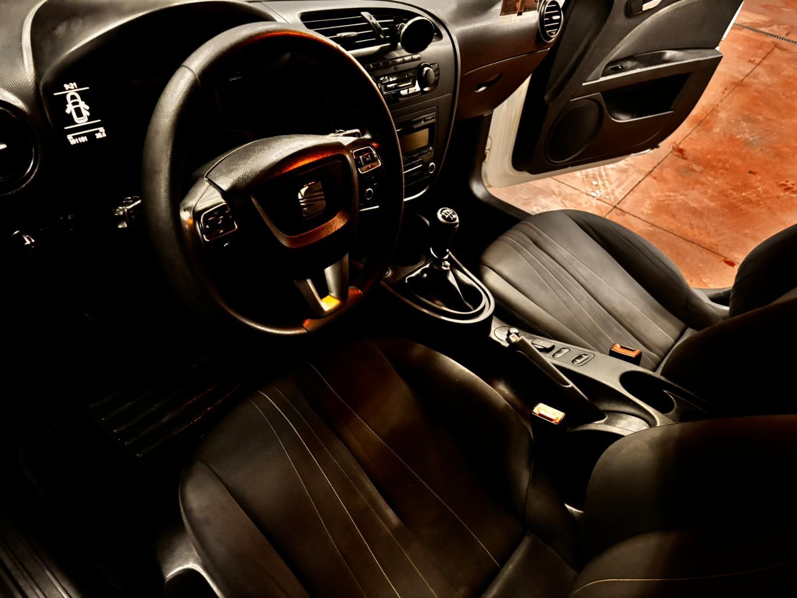 Vista interior del habitáculo de un coche moderno con asientos de cuero negro, volante y salpicadero oscuro.