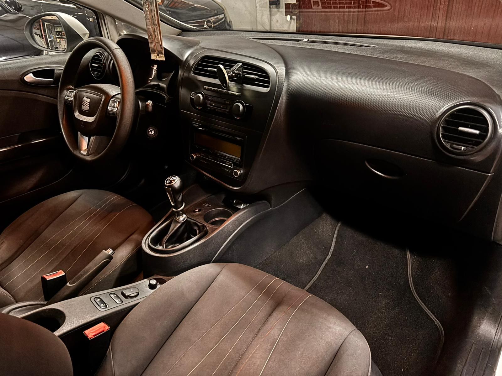 El interior de un coche, donde se aprecian el volante, el salpicadero, la palanca de cambios y los asientos delanteros tapizados en color marrón.