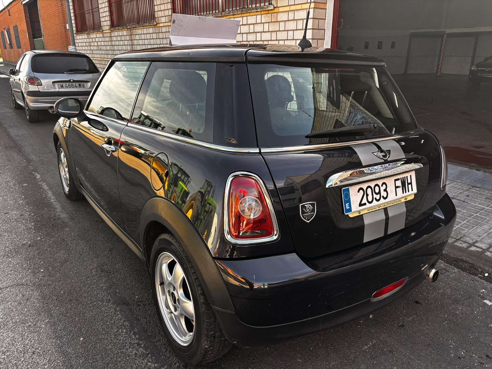 Un Mini Cooper negro estacionado en una calle con franjas de carreras plateadas en la parte trasera, mostrado desde un ángulo de tres cuartos trasero.