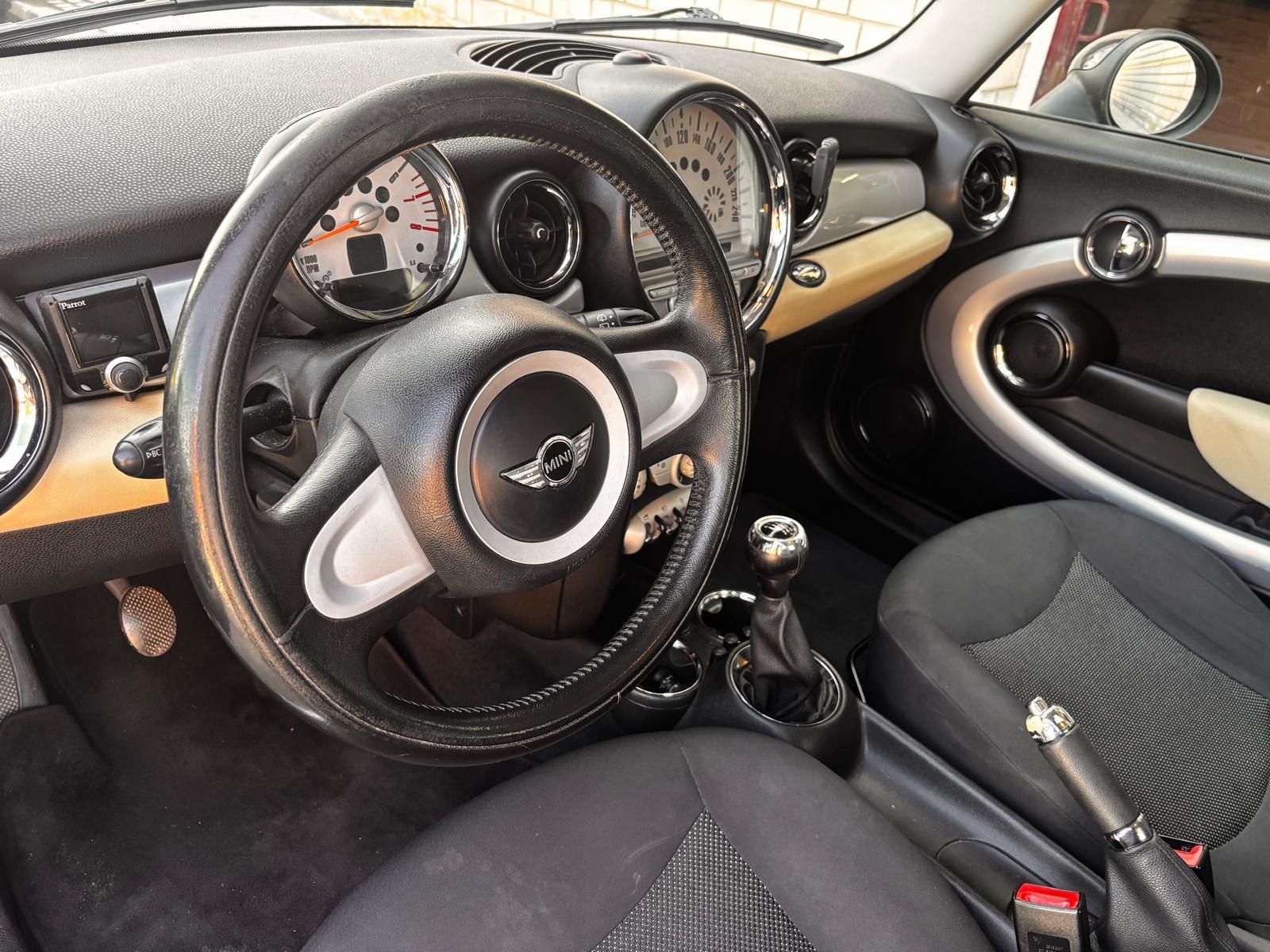Vista interior de un Mini Cooper con volante de cuero negro, asientos de tela y palanca de cambios manual.