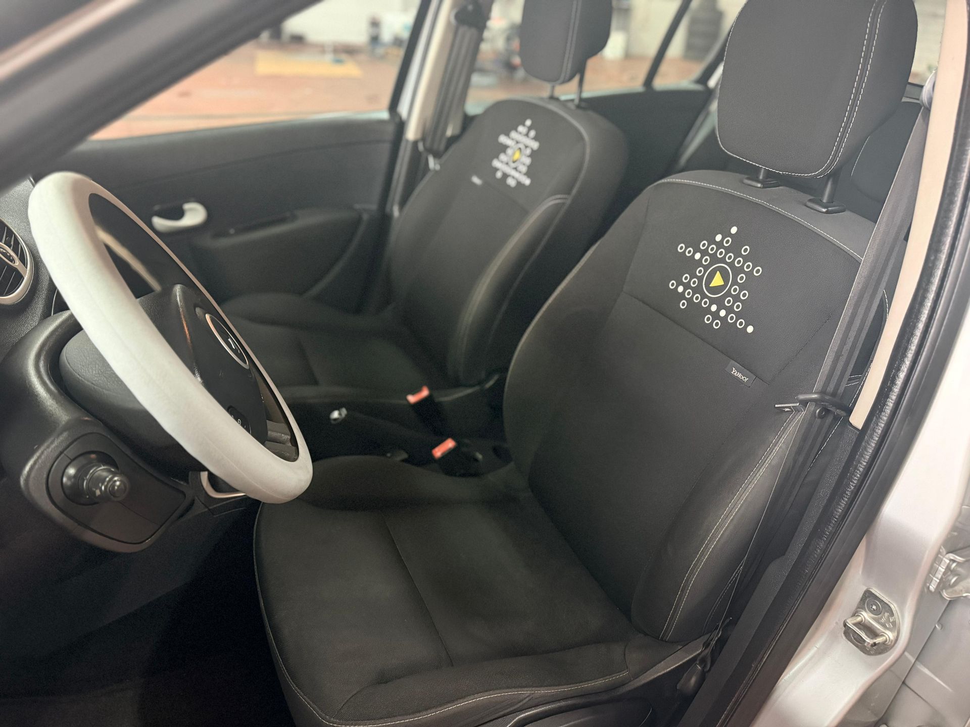 El interior del coche cuenta con asientos delanteros de tela oscura con costuras decorativas blancas y una funda blanca para el volante.