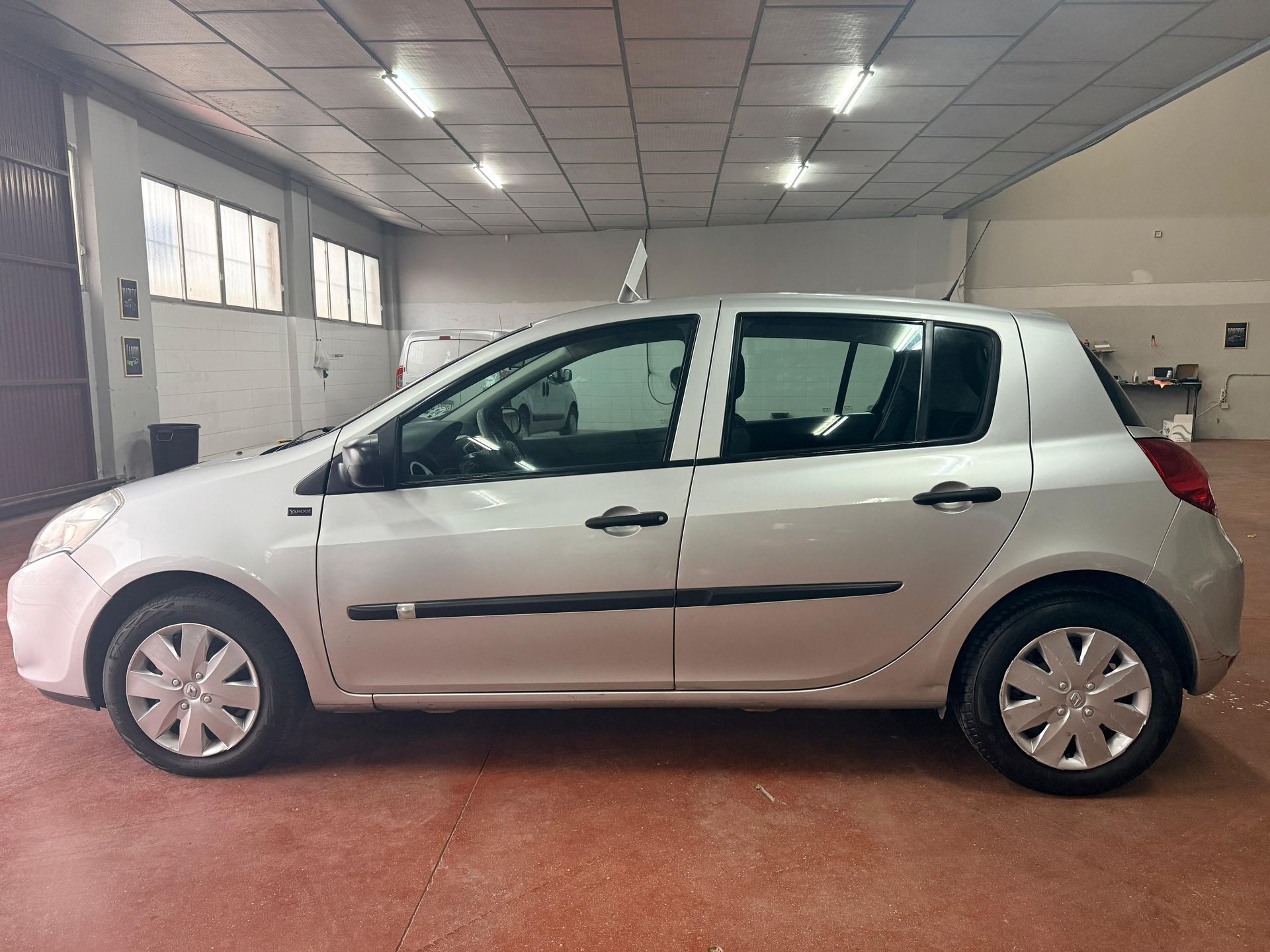 Un coche compacto plateado aparcado en un garaje interior amplio y luminoso con techo de baldosas.