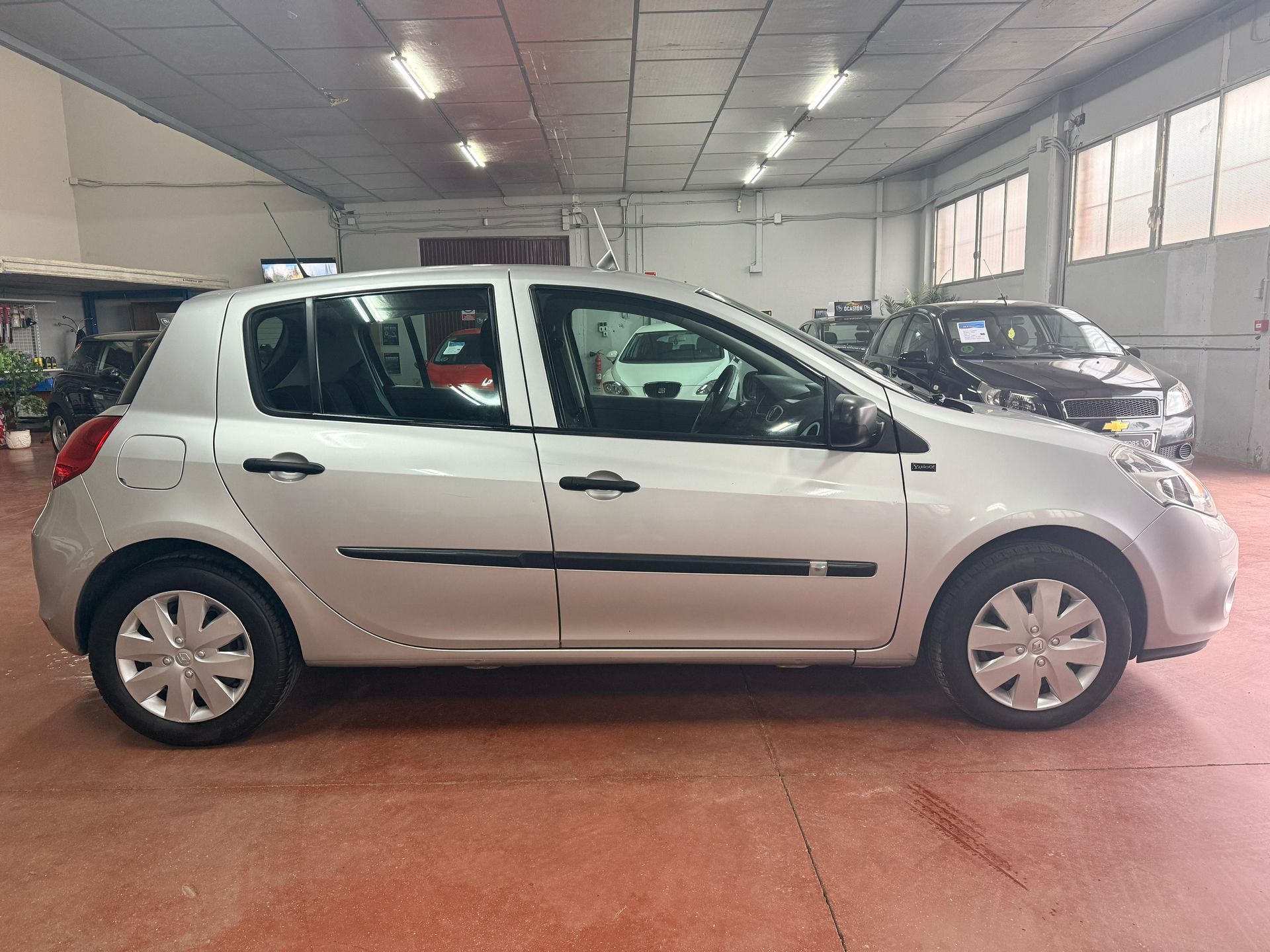 Un coche compacto plateado de cinco puertas aparcado dentro de una sala de exposición interior muy iluminada.