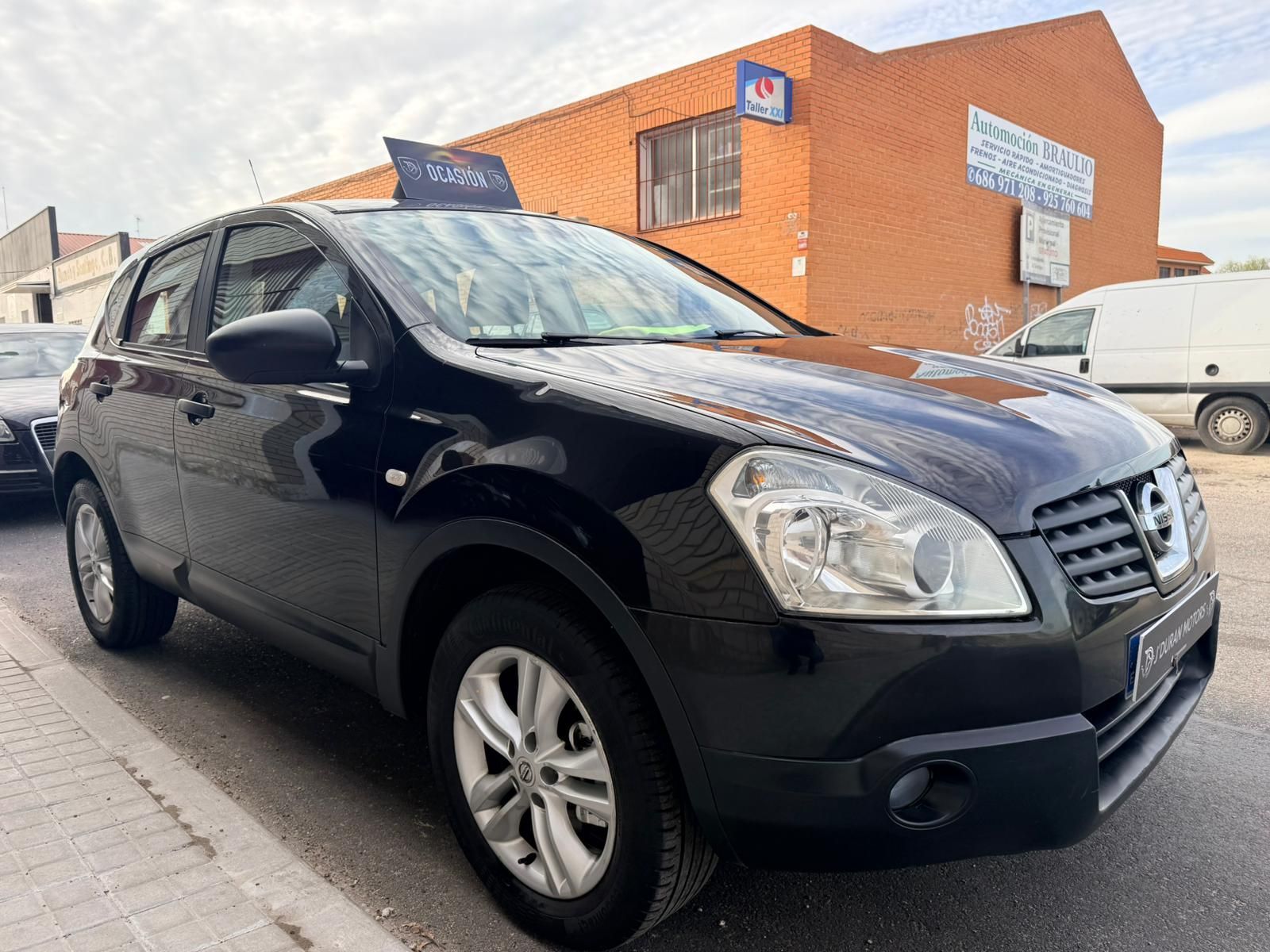 Un SUV Nissan Qashqai negro estacionado en una acera frente a un edificio de ladrillo.