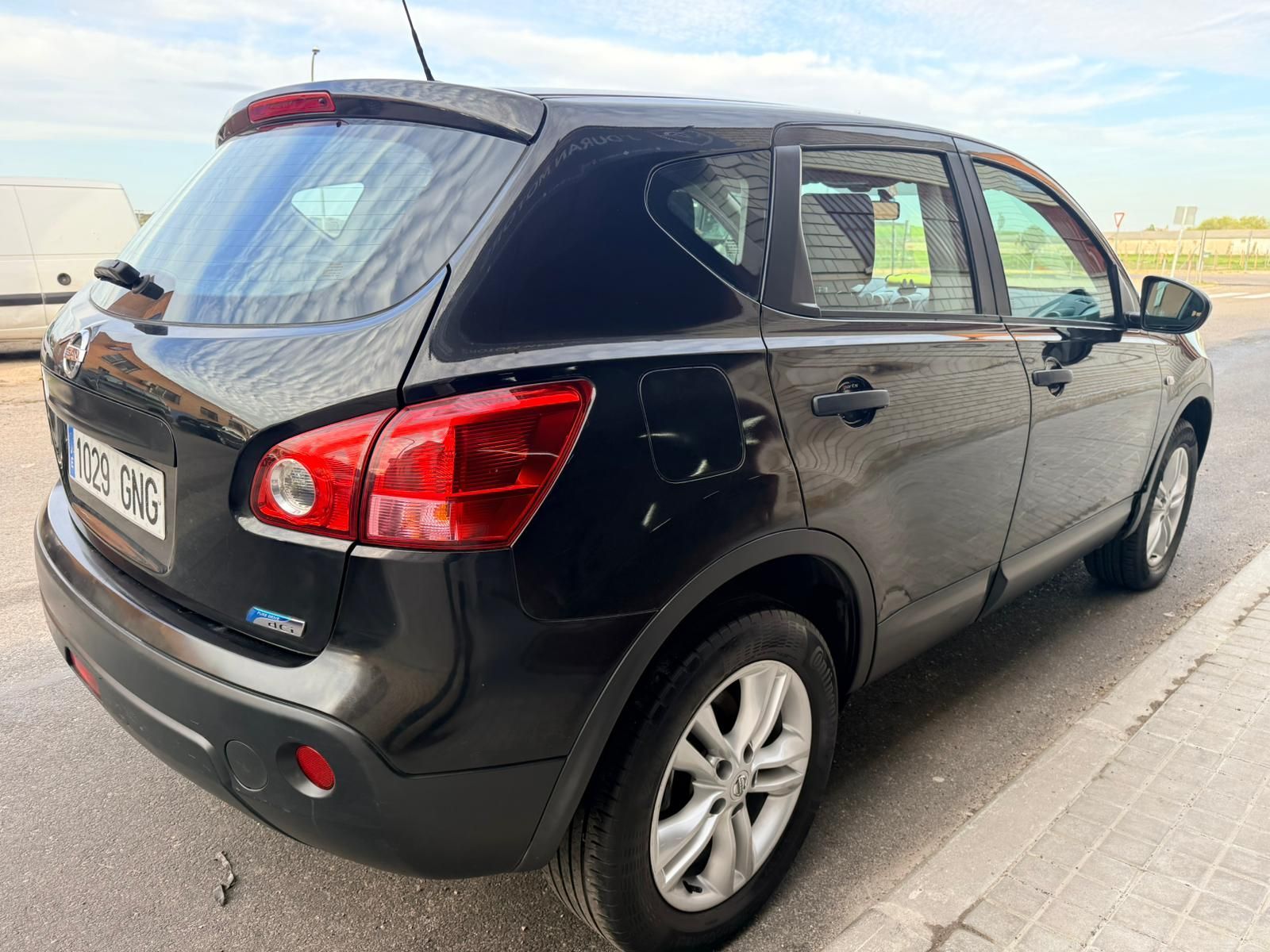 Un Nissan Qashqai negro estacionado en una calle asfaltada, visto desde un ángulo de tres cuartos trasero.