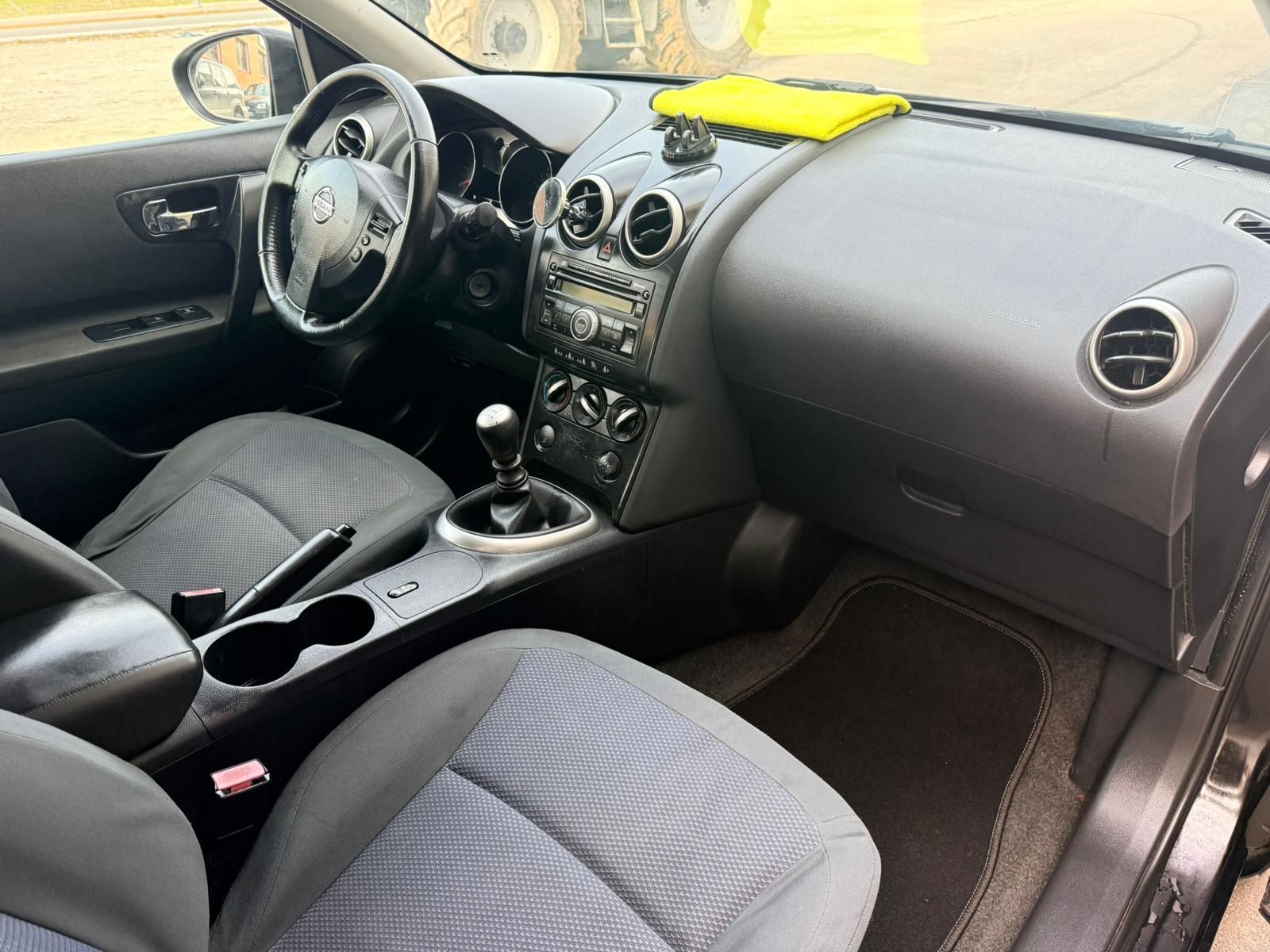 Interior de un coche que muestra asientos de tela gris, un salpicadero negro, una palanca de cambios y una tela amarilla en la consola.