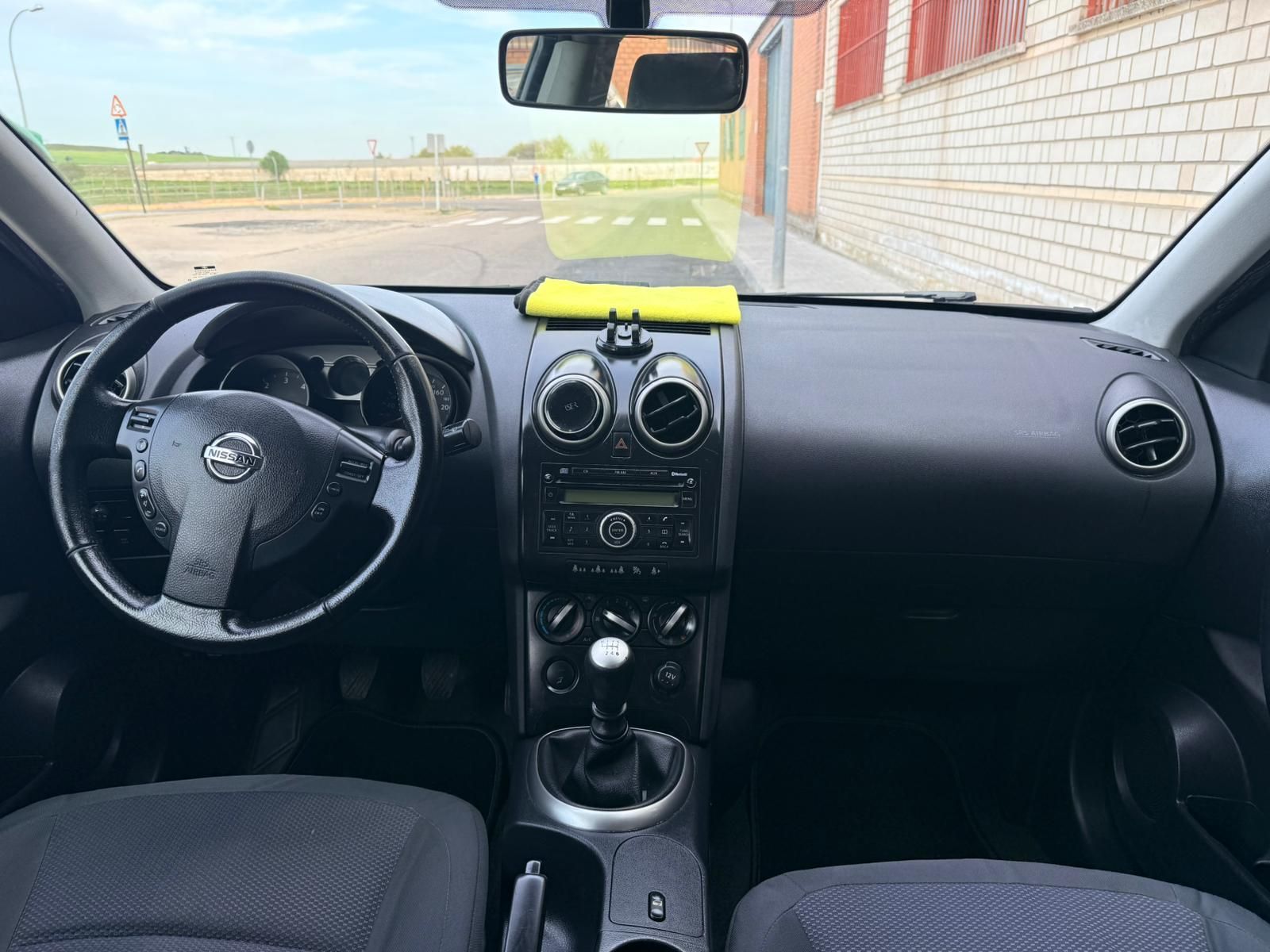 Vista interior del salpicadero de un Nissan Qashqai con volante, palanca de cambios y una tela amarilla brillante en el salpicadero.