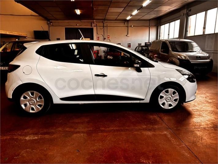 Renault Clio blanco aparcado en el interior de un garaje con suelo rojo, junto a otros vehículos.