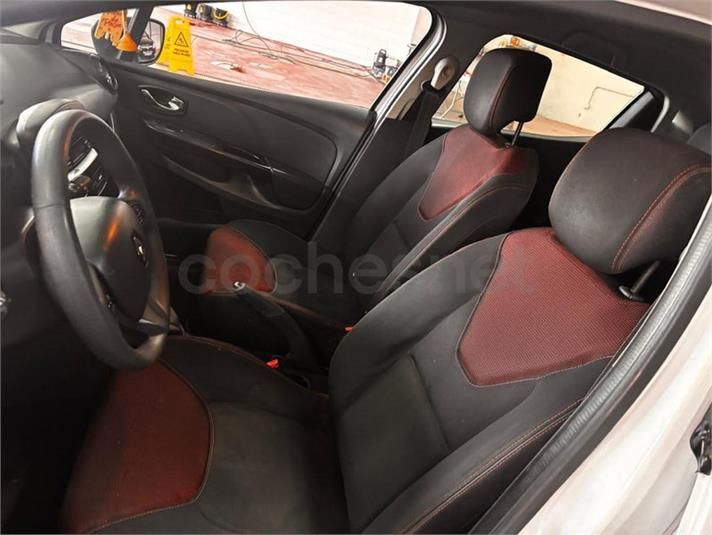 Interior del coche con asientos negros y rojos, volante, tablero visible.