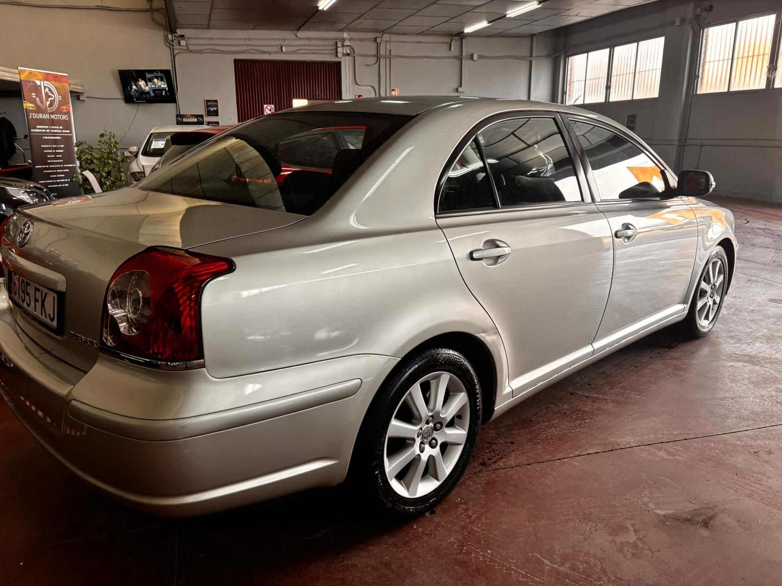 Un sedán plateado estacionado dentro de un garaje con piso de concreto rojo.