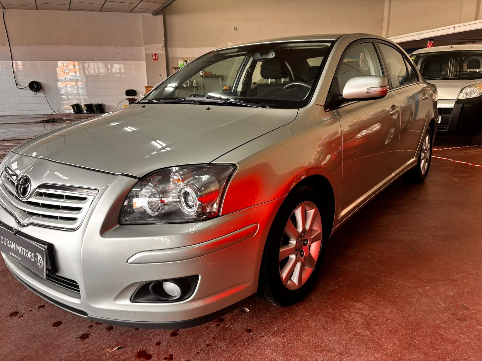 Un sedán Toyota Avensis plateado estacionado en una luminosa instalación automotriz cubierta.