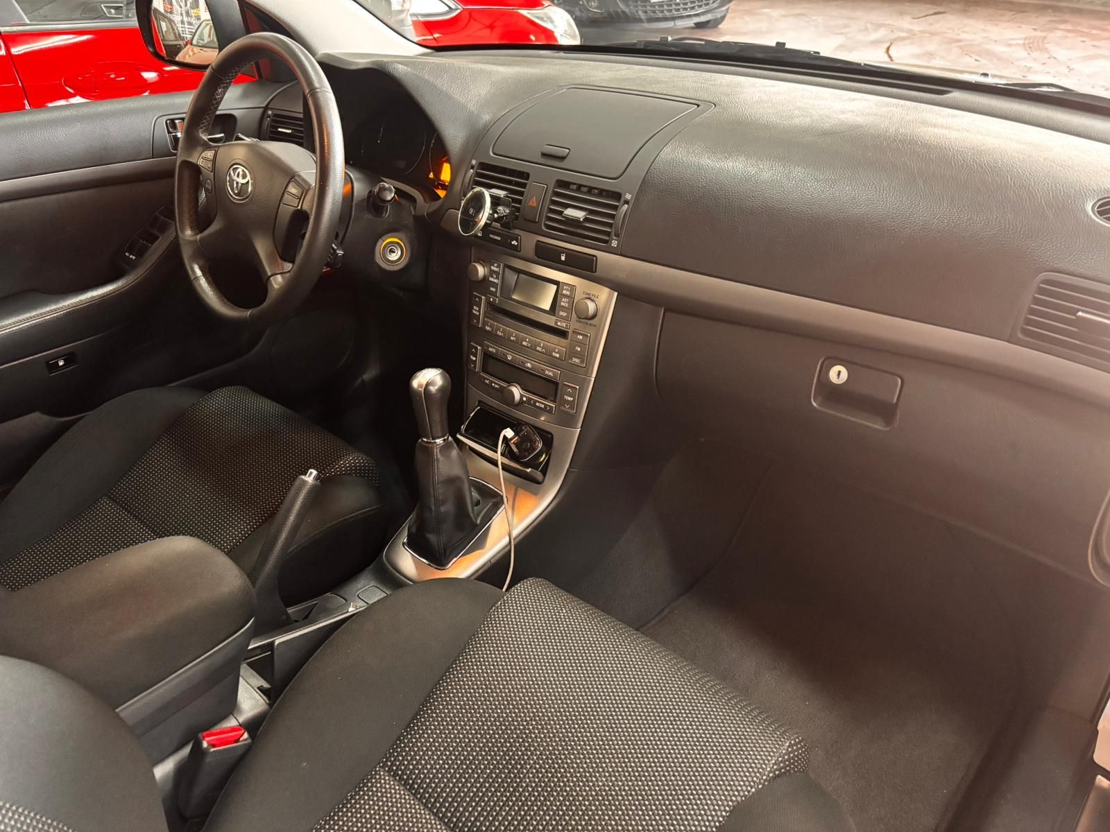 El interior de un automóvil Toyota, donde se aprecian el volante, la consola central con la palanca de cambios y los asientos tapizados en color oscuro.