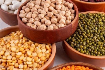 Cuencos de madera llenos de diversas legumbres secas, como garbanzos, guisantes amarillos partidos y frijoles mungo verdes.