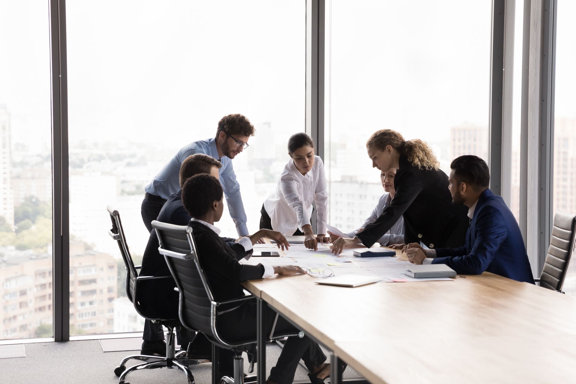 people in a meeting room sitting around table and looking at documents
