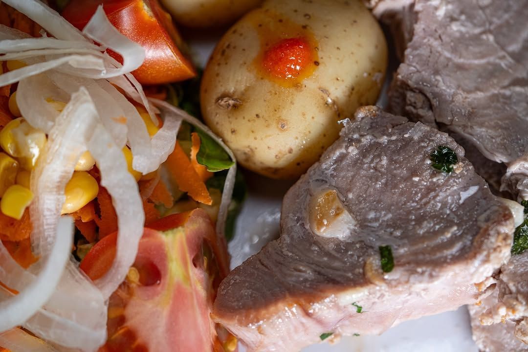 Primer plano de un plato con carne en rodajas, patatas, tomate y cebolla como guarnición.